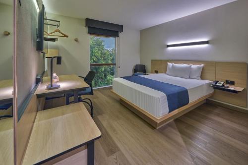 a bedroom with a bed and a desk and a window at City Express by Marriott Playa del Carmen in Playa del Carmen