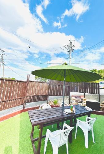 a wooden table with a green umbrella and chairs at ペンションはなはな in Gushichan