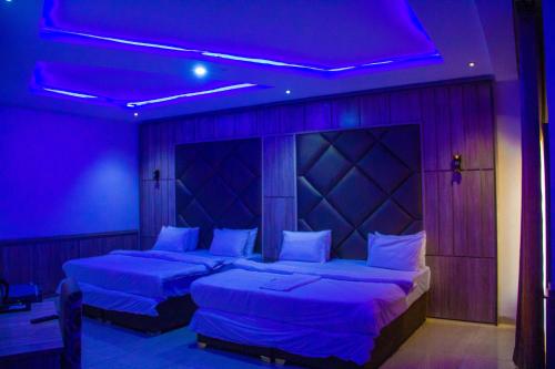 2 camas en una habitación con iluminación púrpura en Emperor Melanie Hotels, en Akwa