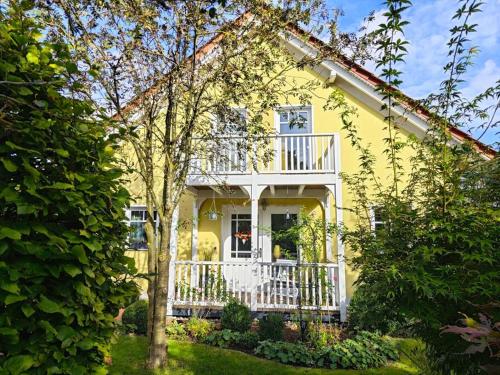 une maison jaune avec une véranda blanche et des arbres dans l'établissement FeWo Hope, à Lindwedel
