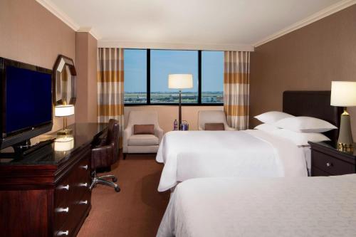 a hotel room with two beds and a flat screen tv at Sheraton DFW Airport Hotel in Irving