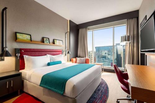 a hotel room with a bed and a desk and a window at Ramada Encore Al Khobar Corniche in Al Khobar