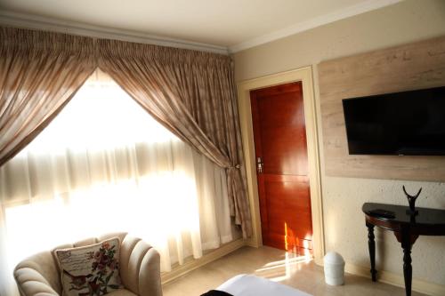 a living room with a couch and a television and a window at The Edge Lodge in Polokwane