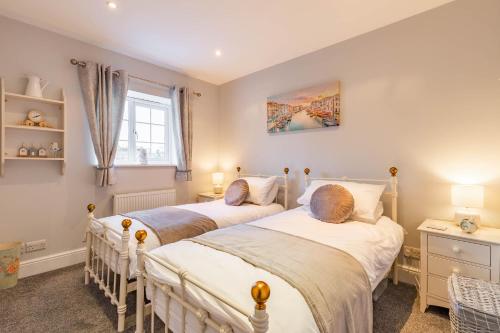 two beds in a bedroom with two lamps and a window at Dibley Cottage Mundesley in Mundesley