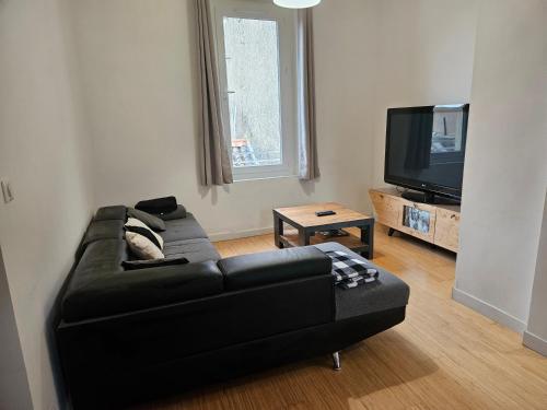 un soggiorno con divano nero e TV a schermo piatto di Appartement Morgand a Narbonne