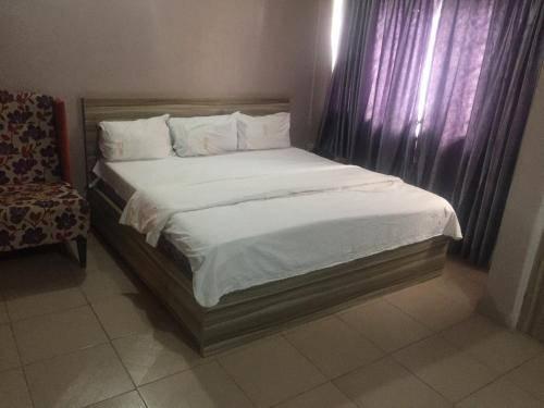 Una cama con sábanas blancas y una silla en una habitación en ClinClia Hotel2, en Ibadán