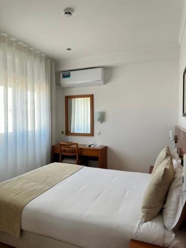 a bedroom with a large white bed and a desk at Europeia Hotel in Caldas da Rainha