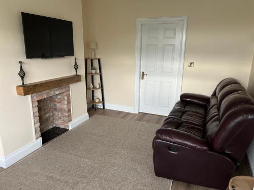 a living room with a leather couch and a fireplace at Milltown Cottage in Aghanloo