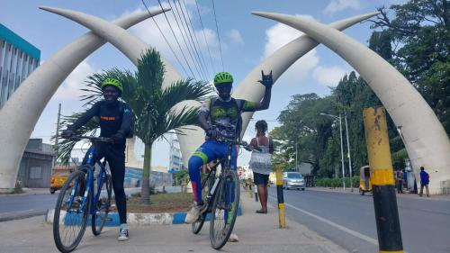 two men riding bikes down a street with their hand in the air at Roma Stays - Splendid Kariba at Sunset Paradise Shanzu with a Swimming Pool in Mombasa