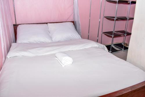 Una cama con sábanas blancas y un rollo. en Minari Holiday Homes, en Bungoma