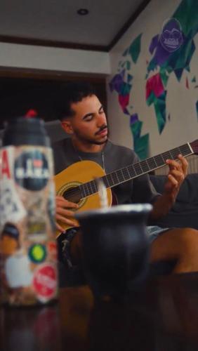 a man playing a guitar in front of a table at Gorilla Hostel in Mendoza
