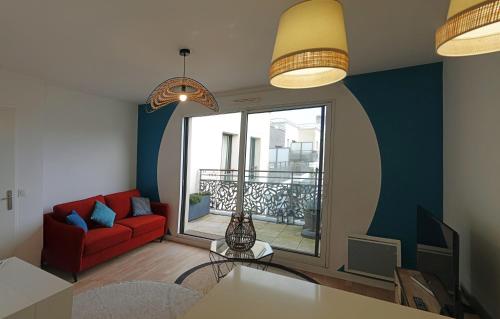 a living room with a red couch and a large window at Appartement résidence neuve proche Versailles in Saint-Cyr-lʼÉcole