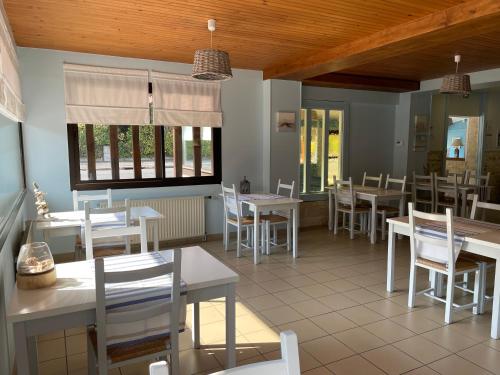 un restaurante con mesas y sillas blancas y ventanas en Le Vauban en Merville-Franceville-Plage