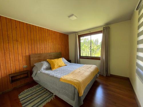 1 dormitorio con cama con almohada amarilla y ventana en Cabaña Curacautín “Refugio Cautin”, en Curacautín