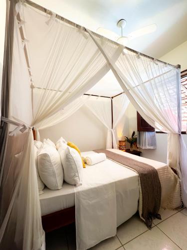 1 dormitorio con cama con dosel, sábanas y almohadas blancas en Casa da Cosmira, en Trancoso