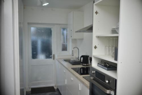 a white kitchen with a sink and a stove at Femros Apartments, 15mins to city center. in Smethwick