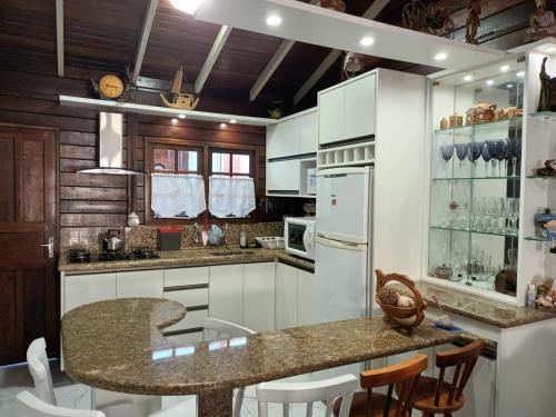 uma cozinha com armários brancos e uma ilha com cadeiras em Casa Agradável, 50m da Praia Freguesia do Ribeirão da Ilha em Florianópolis