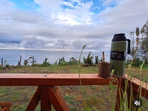 a green thermos sitting on a wooden fence with the ocean at Cabañas Bosquemar 1 in Queilén