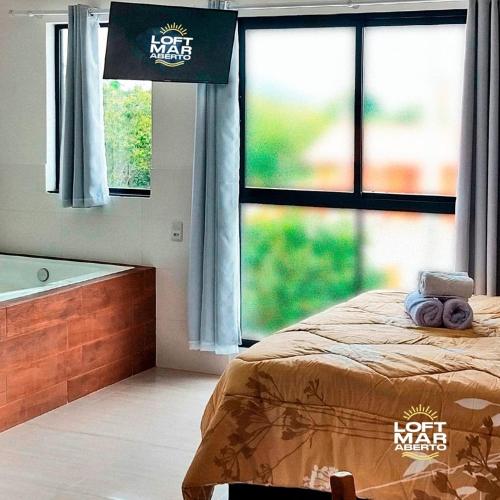 a bedroom with a bed and a tub and windows at Charmoso Loft #1 próximo da praia com banheira in Pinheira