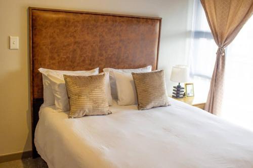 1 cama con almohadas blancas y cabecero de madera en 8 Elizabeth Place - Luxury Apartments , Free Wi-Fi, en Midrand