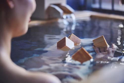 a woman in a bathtub with wooden blocks in the water at Hotel Indigo Hakone Gora by IHG in Hakone