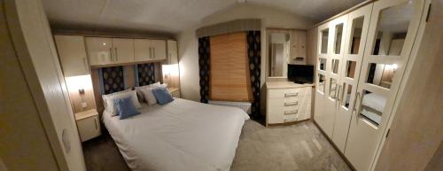 a small bedroom with a white bed with blue pillows at Golden Anchor Caravan Park, Europa Sequoia Private Static Caravan Hire on Wildflower Meadow in Chapel Saint Leonards
