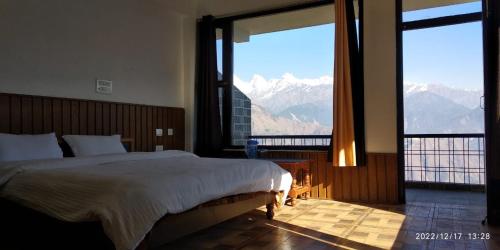 Schlafzimmer mit einem Bett und einem großen Fenster mit Bergblick in der Unterkunft Hotel Milam Inn in Munsyari