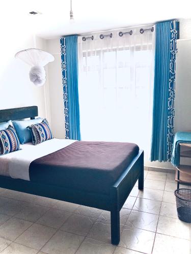 a bedroom with a bed with blue curtains and a window at Gem in Busia