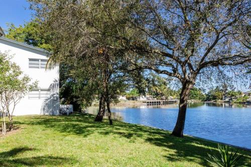 a house with trees in the grass next to a lake at Stylish - Water View Condo - Palm Wave Says in Coconut Creek
