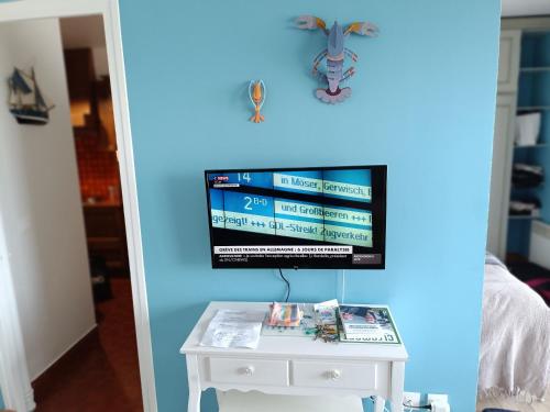 a tv on a blue wall next to a white table at Cabourg Face A La Mer in Cabourg