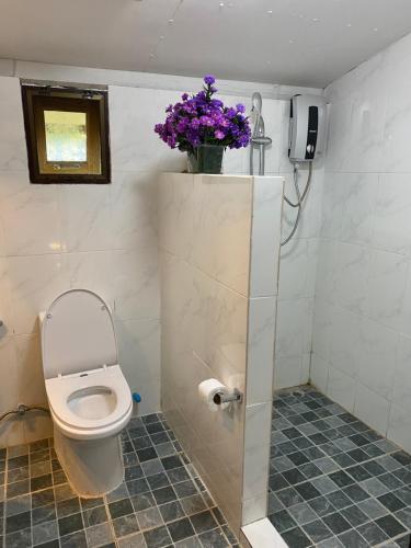 La salle de bains est pourvue de toilettes et d'un vase de fleurs violettes. dans l'établissement Cozycomo Chiang Dao - Pha Mok, à Amphoe Chiang Dao