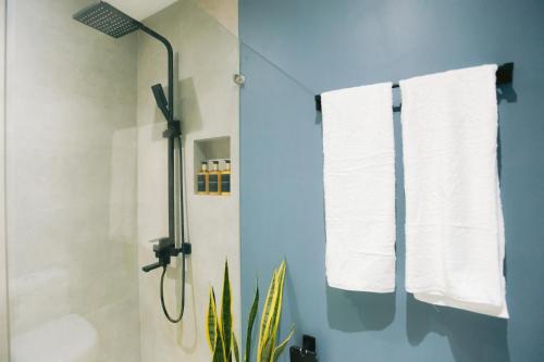 ein Badezimmer mit einer Dusche, weißen Handtüchern und einer Pflanze in der Unterkunft 10 Oxford Residences in Quezon City