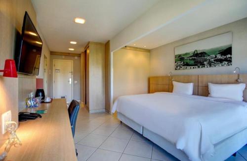 1 dormitorio con 1 cama blanca grande y escritorio en Suíte Autônoma Quality Barra en Río de Janeiro