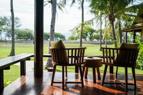 two chairs and a table on a porch with palm trees at Pondok Santi Estate in Gili Trawangan