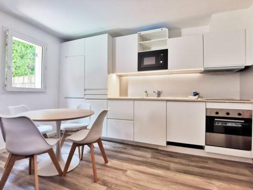 une cuisine avec des armoires blanches et une table et des chaises dans l'établissement Les quatre loges - joli t2 jardinet et parking *3, à Aix-en-Provence