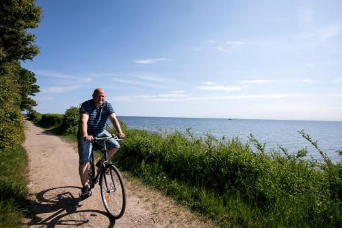 a man riding a bike on a path near the water at Nysted Strand Camping & Cottages in Nysted