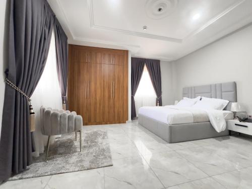 a white bedroom with a bed and a chair at The AUD Luxury Apartments in Kumasi