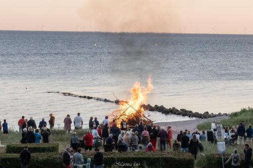 a crowd of people standing around a bonfire by the water at Nysted Strand Camping & Cottages in Nysted