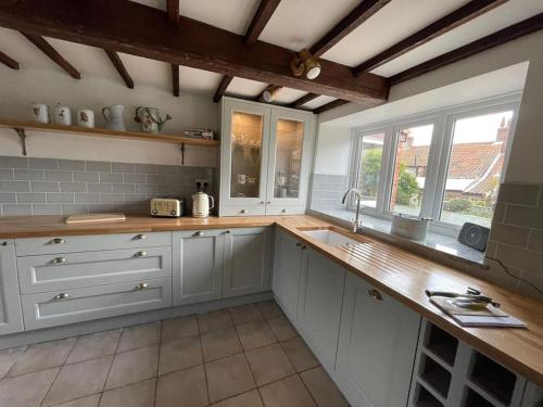 cocina con armarios blancos y encimera de madera en Gardeners Cottage near the Norfolk Coast, en Knapton