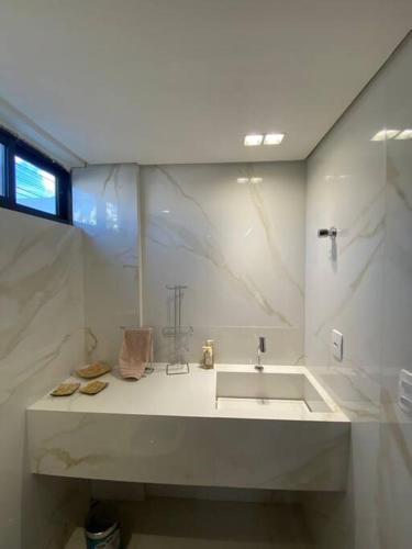 a white bathroom with a sink and a window at Bangalô na praia in Cabedelo