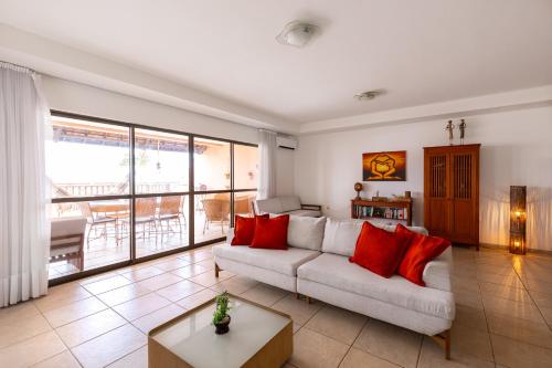 uma sala de estar com um sofá branco e almofadas vermelhas em Oceanview A102 - PÉ NA ÁREA - perto do centro, 2 dormitórios, piscina, cozinha, 116m2 em Cumbuco