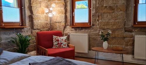 1 dormitorio con silla roja, mesa y ventanas en Ferienwohnung am Bächelweg, en Bad Schandau