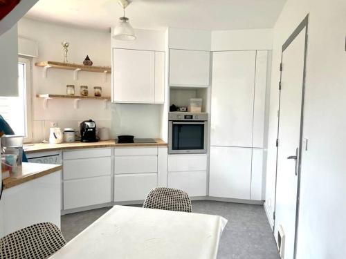 cocina con armarios blancos, mesa y sillas en Maison proche de plage, 3 chambres en La Rochelle