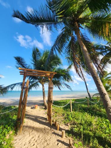 a wooden pergola on a beach with palm trees at Casa Caroá - Chalé 1 in Japaratinga