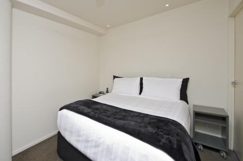 a bedroom with a white bed with a black blanket on it at Pavilion Beachfront Apartments in Mount Maunganui
