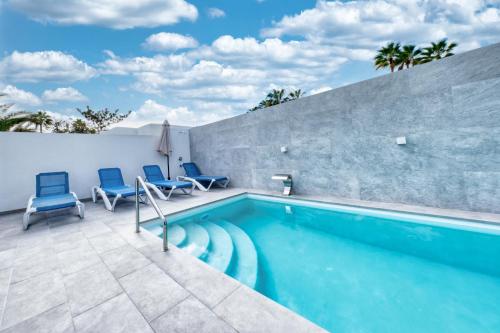 a swimming pool with blue chairs next to a wall at Casa Eva - Private Pool, BBQ & Free Parking By Lanzarote Vacation Homes in Los Pocillos