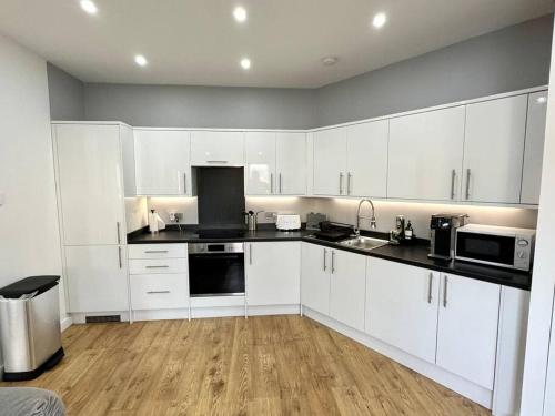 una cucina con armadietti bianchi e ripiani neri di The Modern Smart Home a Great Warley Street