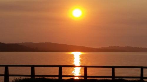 un coucher de soleil sur une étendue d'eau avec une clôture dans l'établissement Hostal Vista al Mar hct, à Ancud