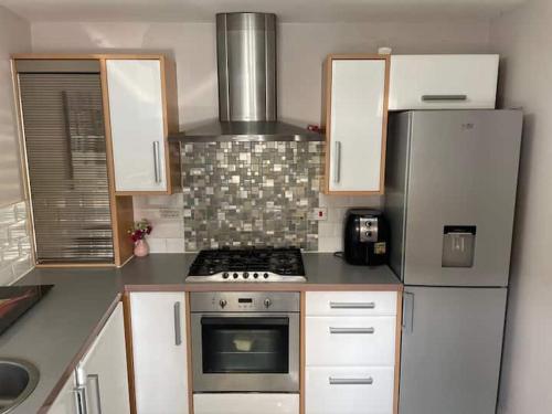een keuken met witte kasten, een fornuis en een koelkast bij The Comfy place Shared in Dallington