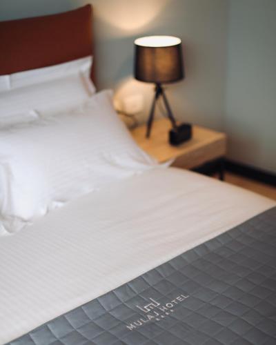 a bed with white sheets and a table with a lamp at Mulaj Hotel in Tirana